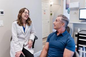 a woman in a lab coat is talking to a man in a dental chair .