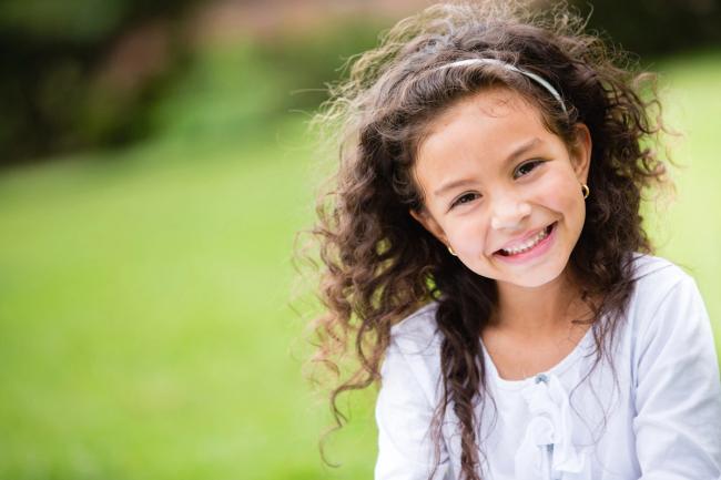 Smiling girl with curly hair and a white headband against a green background.
