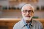 an elderly man with glasses and a beard is smiling for the camera.