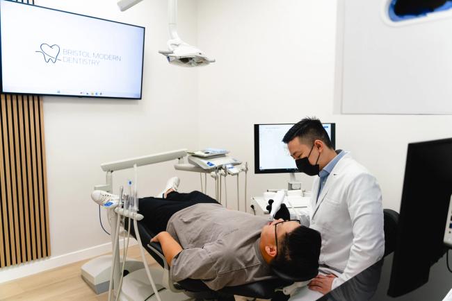 A masked dentist examines a patient in a modern dental office.