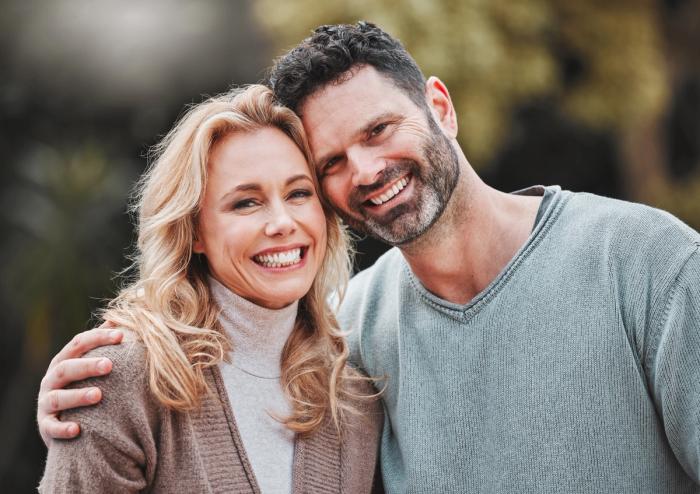 a man and a woman are posing for a picture and smiling for the camera .