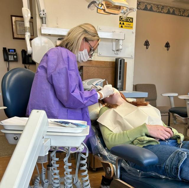 a woman is sitting in a dental chair getting her teeth examined by a dentist .