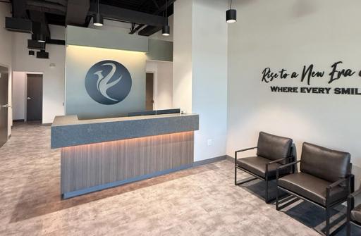 Modern reception area with a lit desk, stylized logo, black waiting chairs, and wall text.