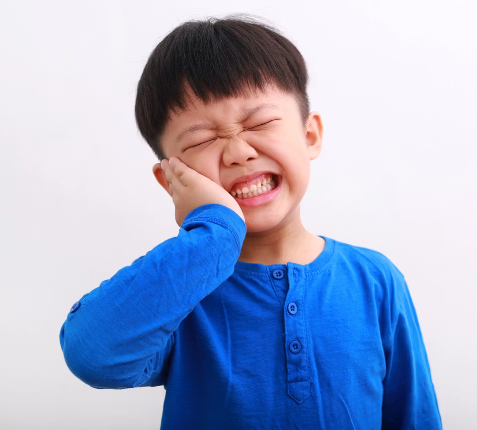 Young boy clutching his cheek with a pained expression.