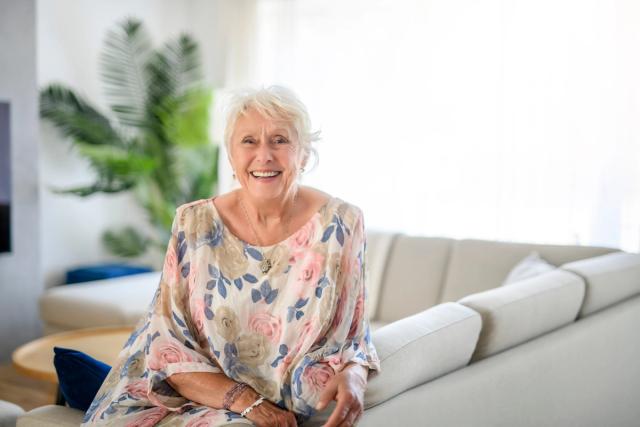 an elderly woman is sitting on a couch in a living room and smiling .