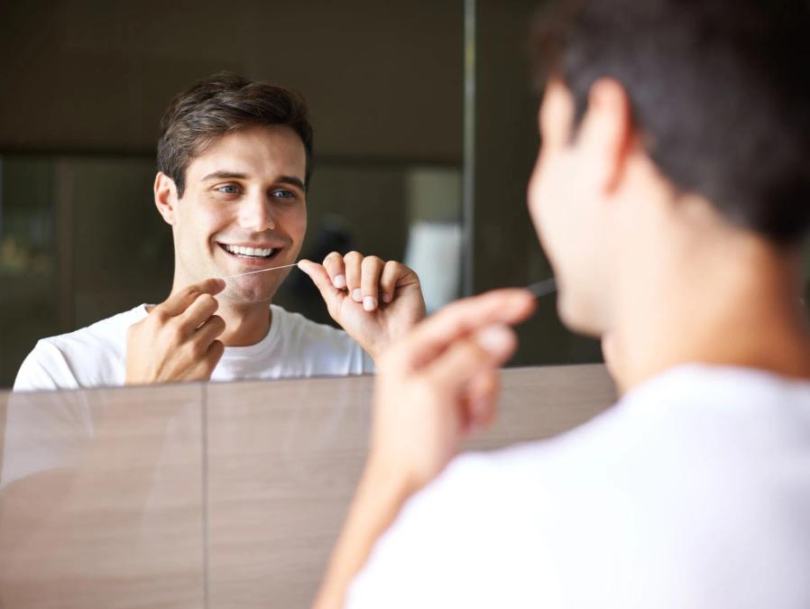 a man is flossing his teeth in front of a mirror .
