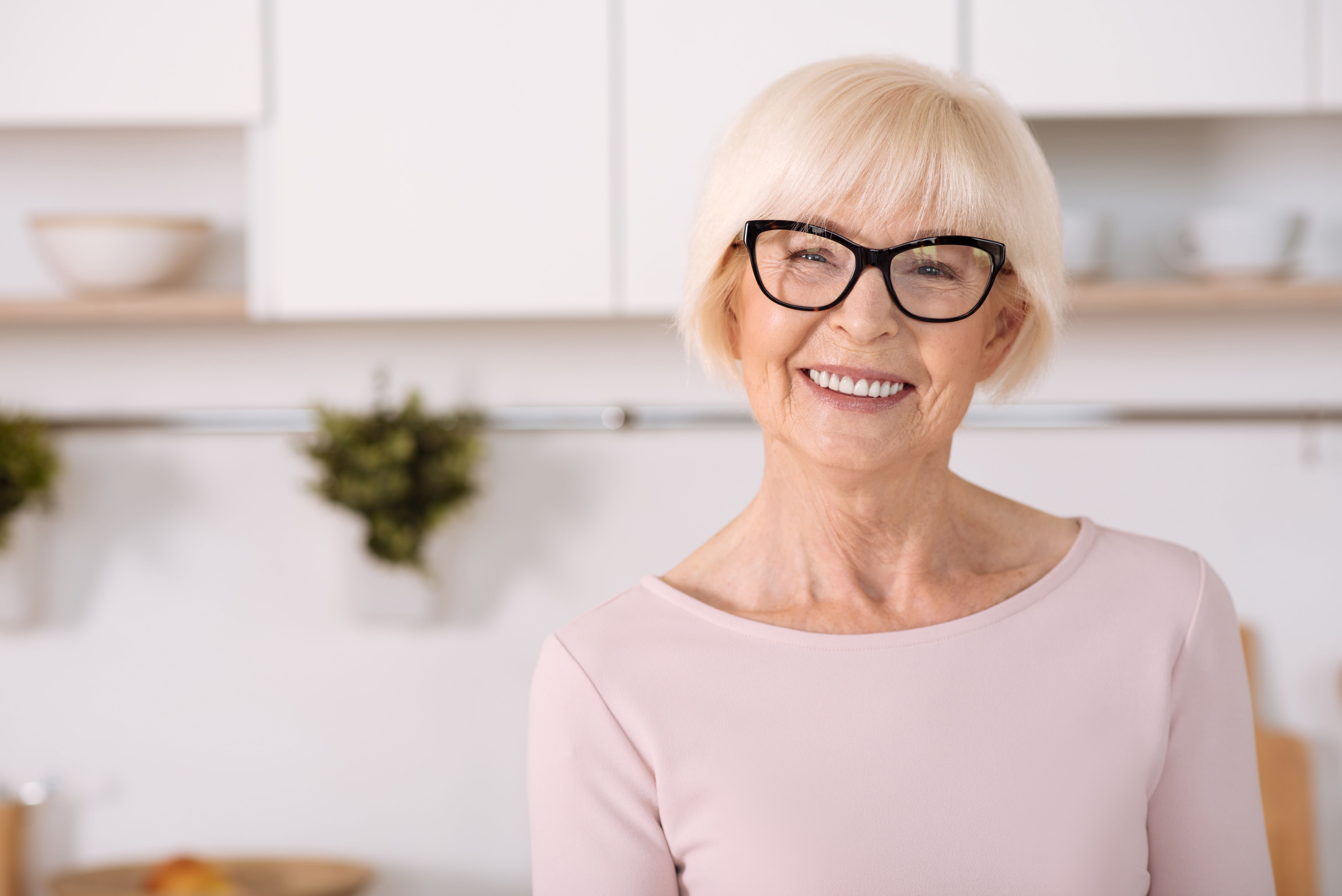 an elderly woman wearing glasses is smiling in a kitchen .