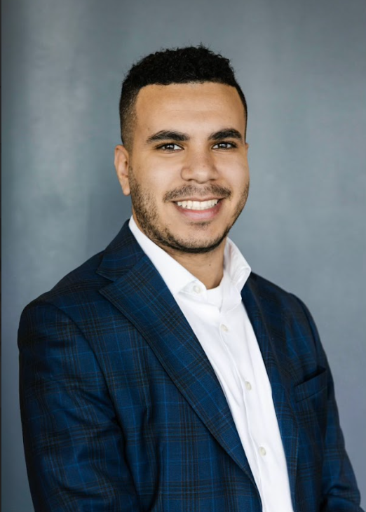 A smiling man in a blue plaid suit and white shirt.