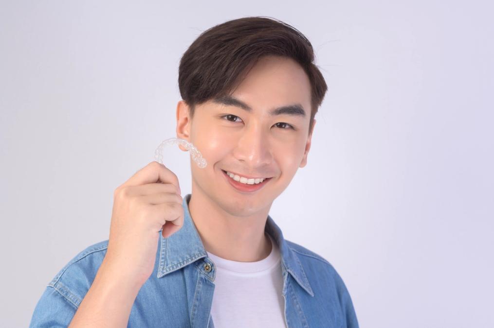 a young man is smiling while holding a clear brace on his teeth .