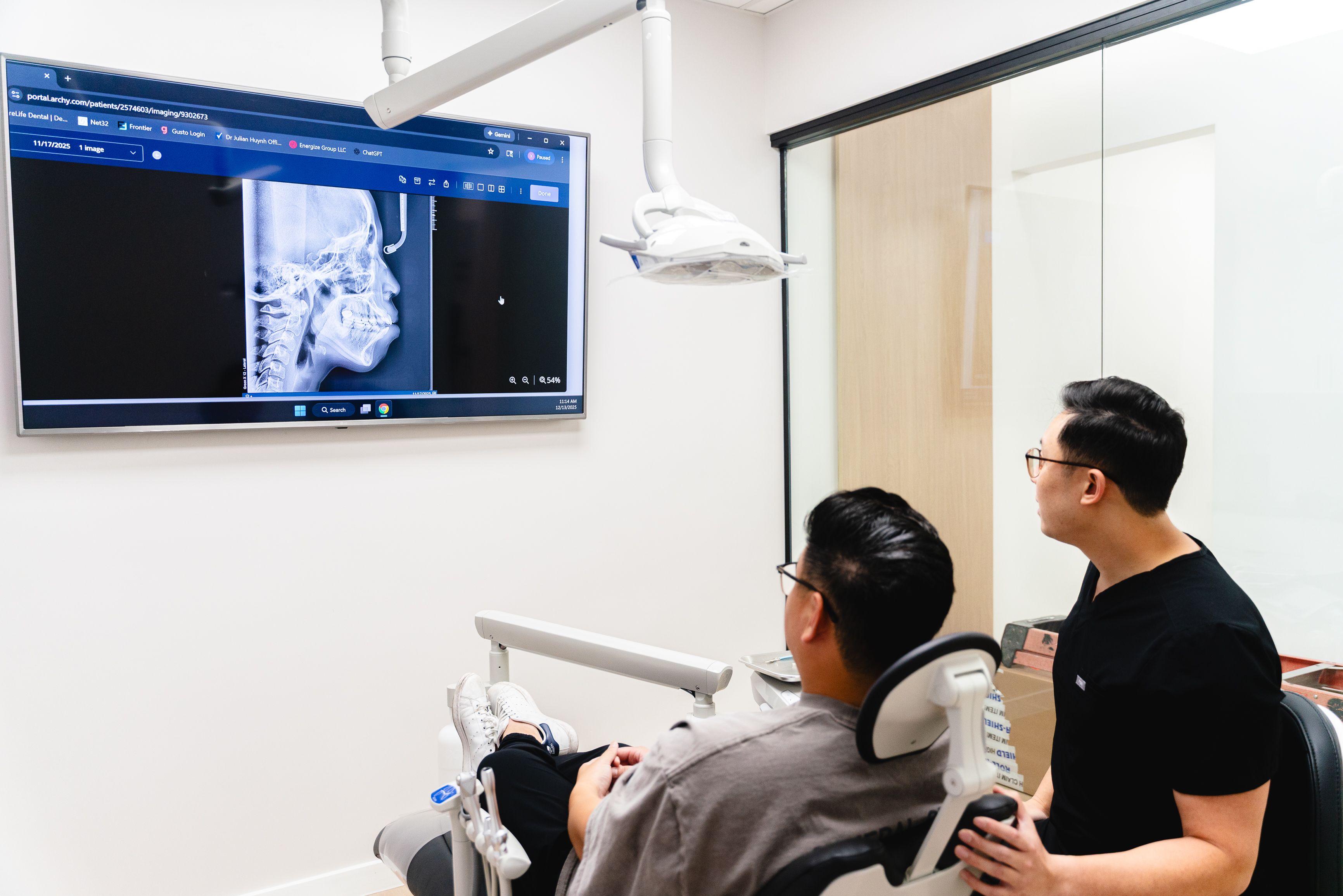A dentist and patient view a dental scan on a wall screen.