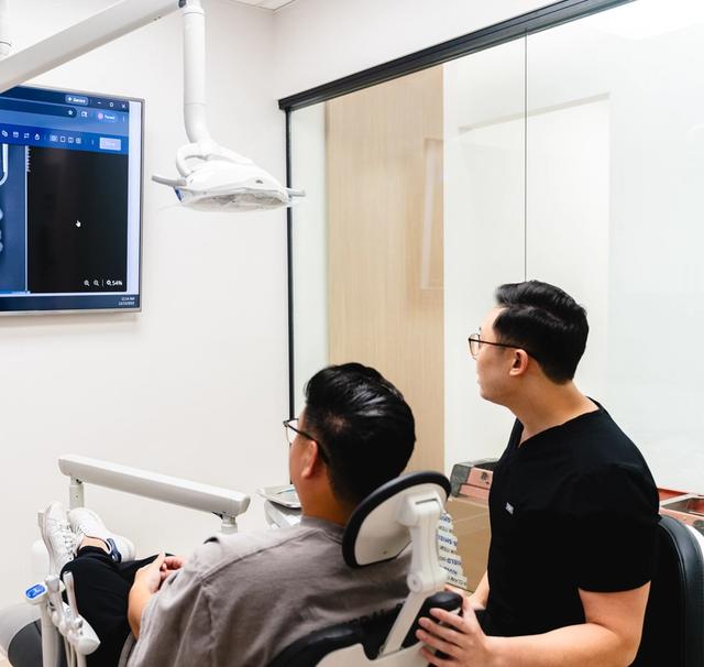 A dentist and patient view a dental scan on a wall screen.