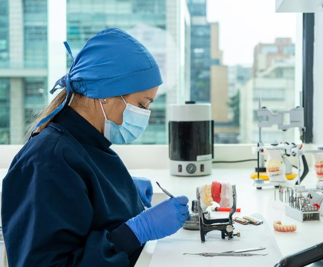 a female dentist is working on a model of teeth in a lab .