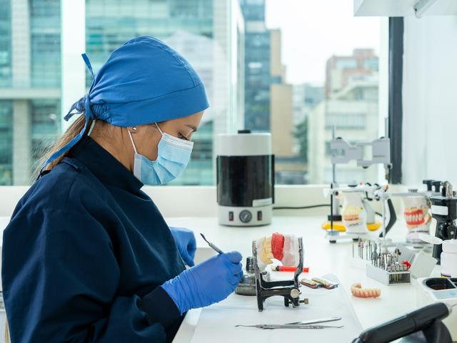 a female dentist is working on a model of teeth in a lab .