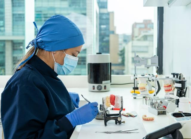 a female dentist is working on a model of teeth in a lab .