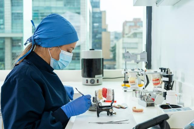 a female dentist is working on a model of teeth in a lab .