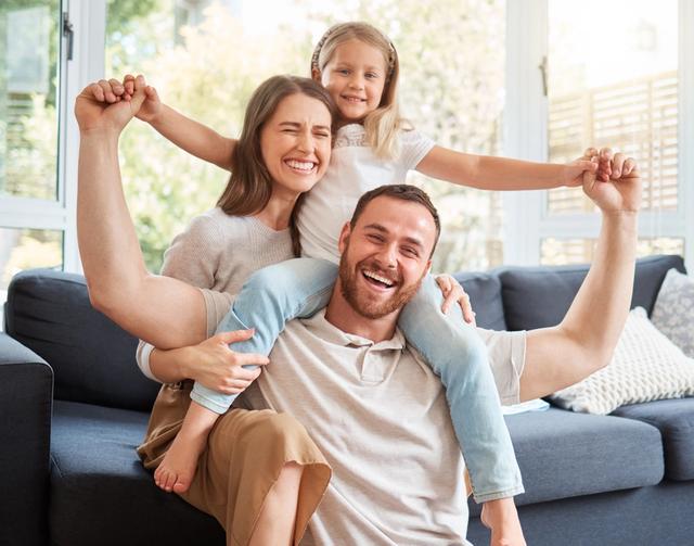 a man is carrying a little girl on his shoulders while sitting on a couch .
