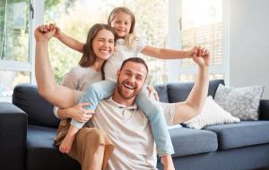 A happy family of three laughing together in a bright living room.