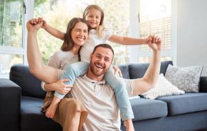 A happy family of three laughing together in a bright living room.