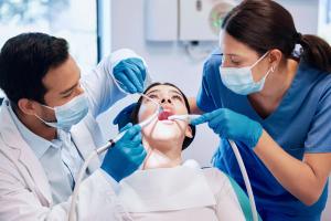 a woman is getting her teeth examined by two dentists in a dental office .