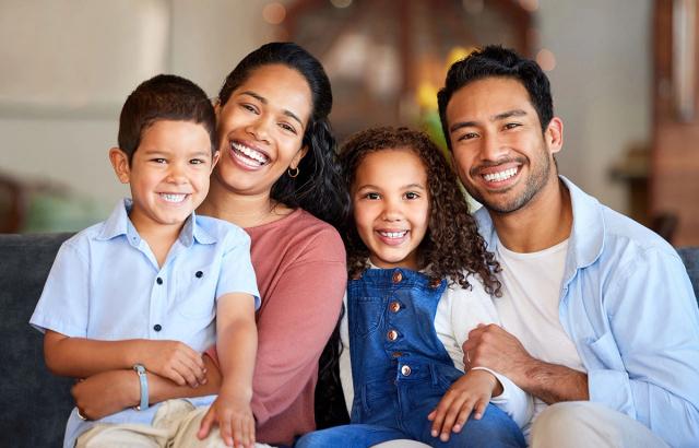 A diverse family of four, including two adults and two children, smiling at the camera.