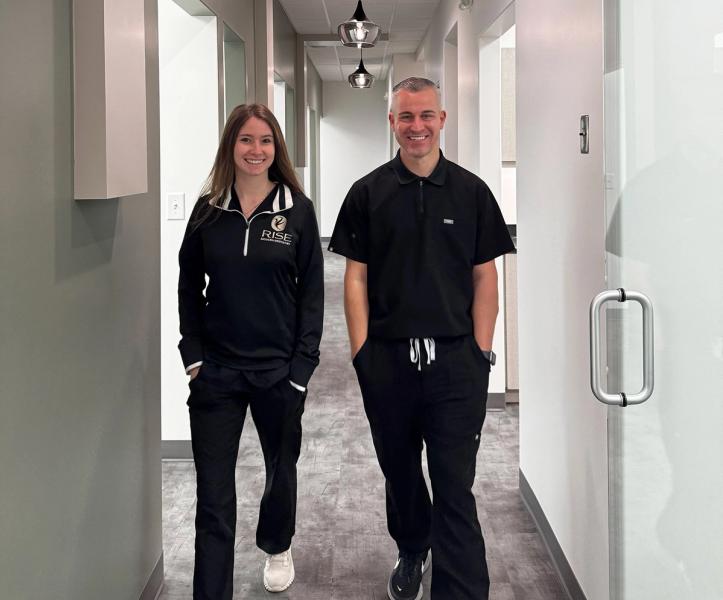 A smiling man and woman in black uniforms walk down a modern hallway.