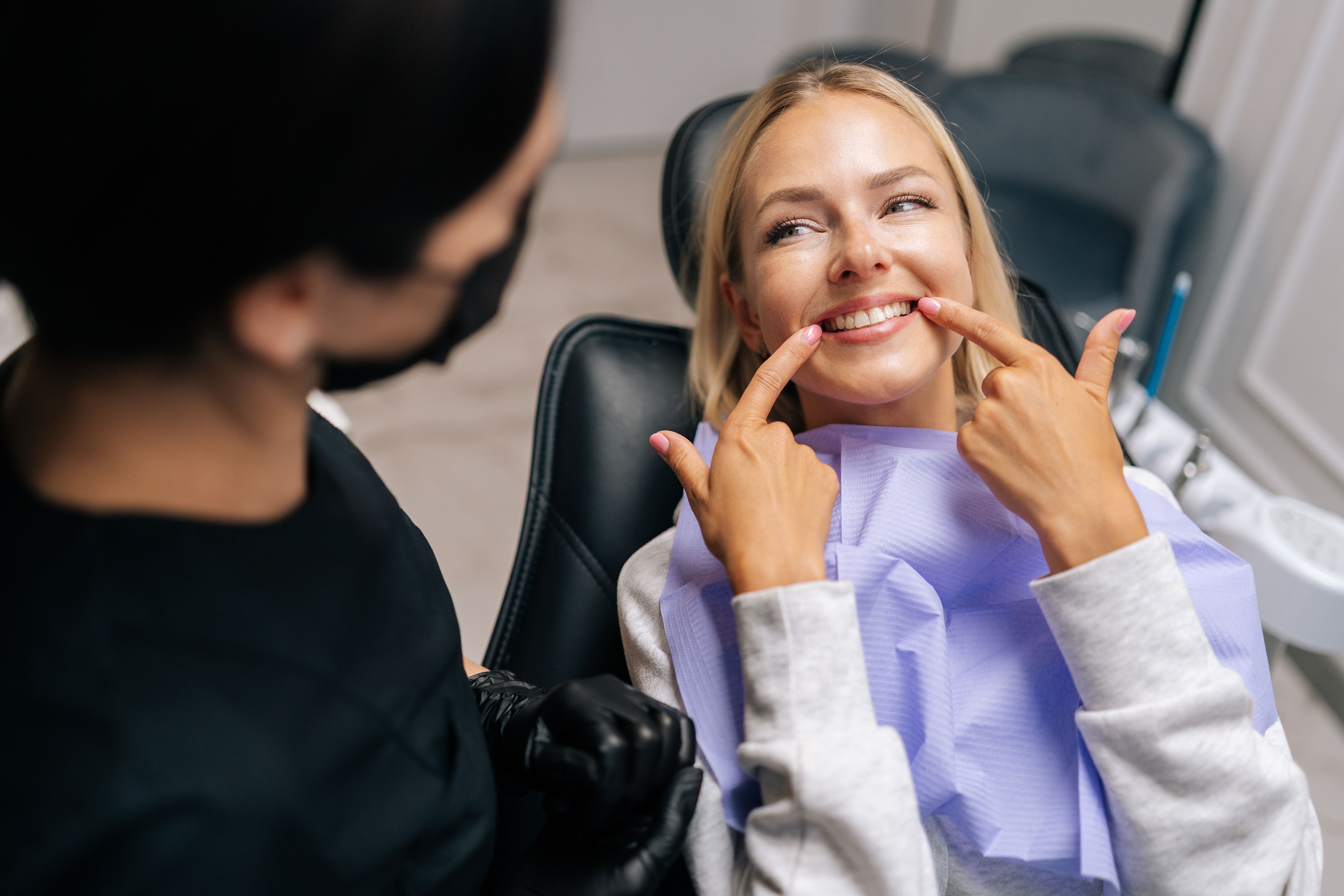 a woman is sitting in a dental chair and pointing at her teeth .