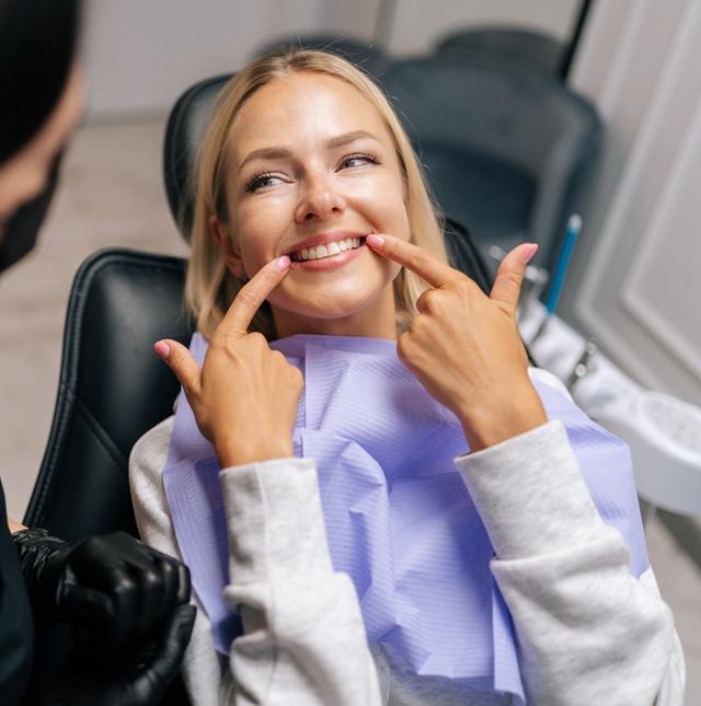 a woman is sitting in a dental chair and pointing at her teeth .