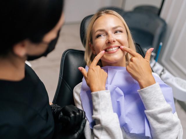 a woman is sitting in a dental chair and pointing at her teeth .