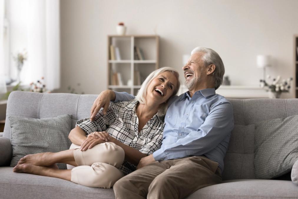 An older couple laughing heartily on a sofa.