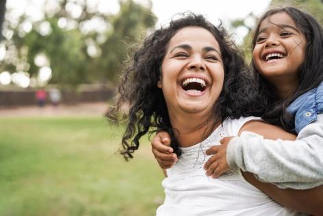a woman is carrying a little girl on her back and they are laughing .