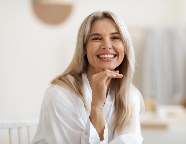 a smiling woman is sitting at a table with her hand on her chin .