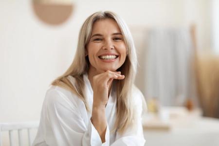 a smiling woman is sitting at a table with her hand on her chin .