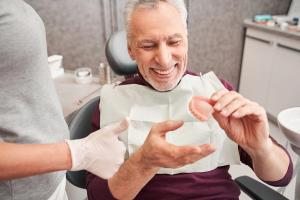 an elderly man is sitting in a dental chair holding a denture .