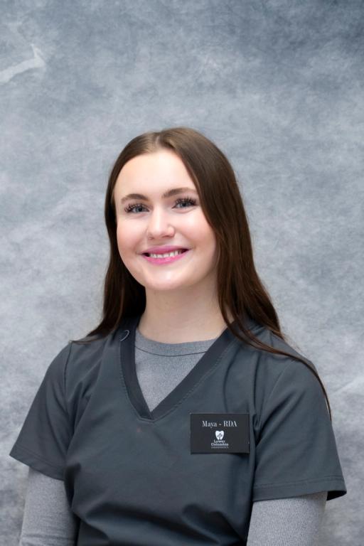 Maya, an RDA from Lowery Cosmetic Dentistry, smiles in grey scrubs against a grey background.