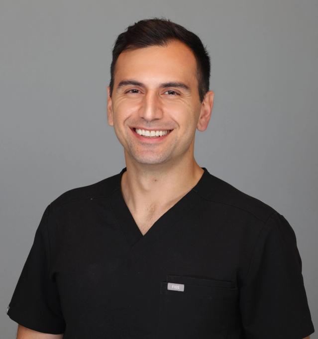 a man wearing a black scrub top is smiling for the camera .