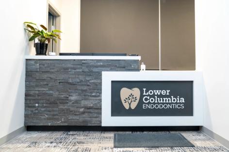 A reception desk with a gray stacked stone front and a sign for "Lower Columbia Endodontics" featuring a tooth and tree logo.