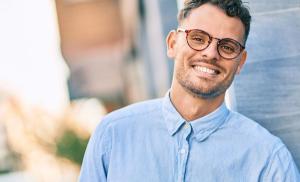 a young man wearing glasses is smiling and leaning against a wall .