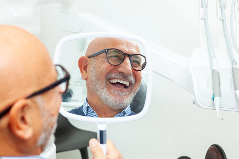 a man is looking at his smile in a mirror at the dentist.