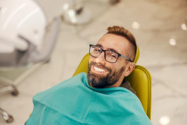 a man with glasses is smiling while sitting in a dental chair .