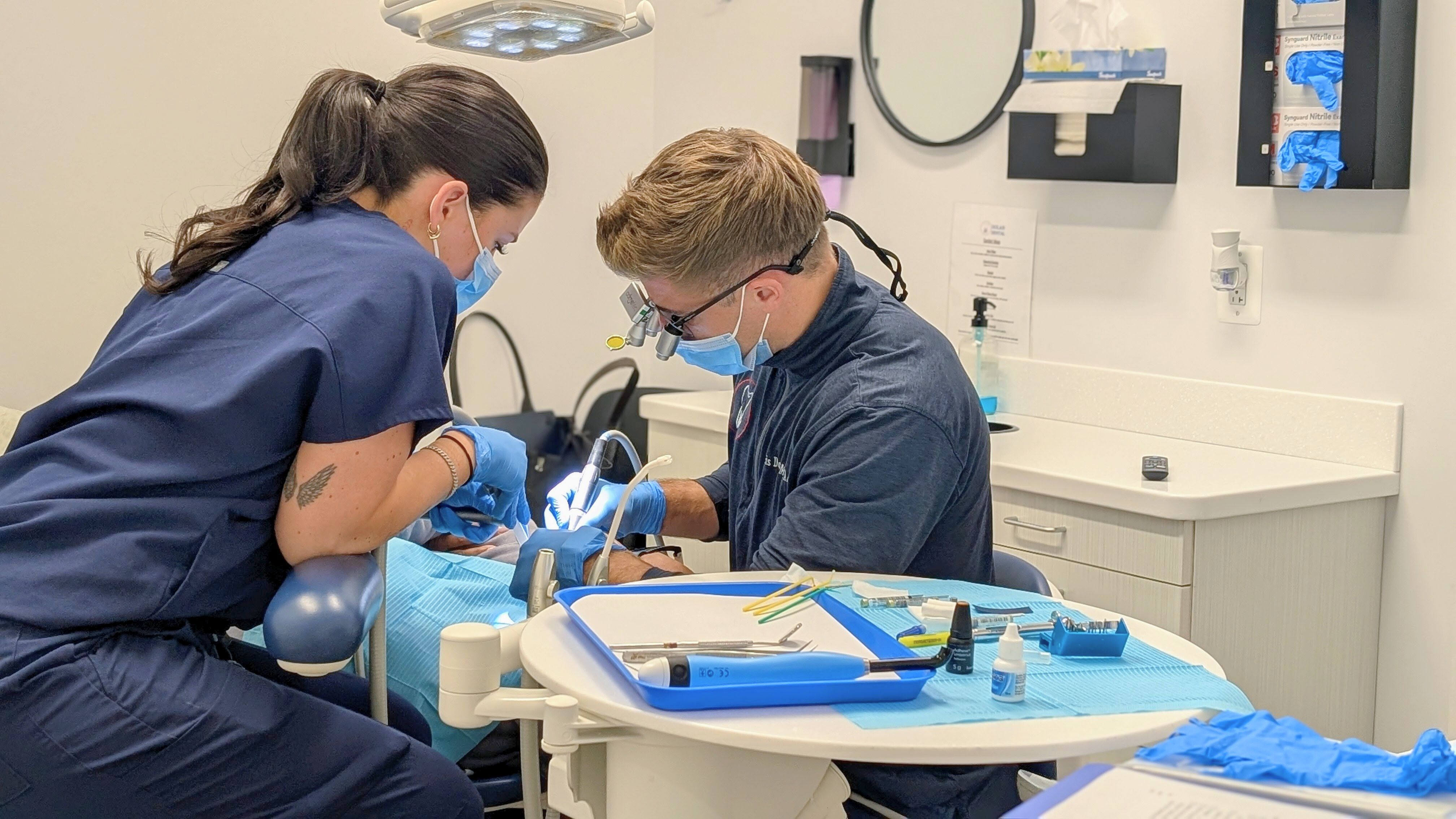 a man and a woman are working on a patient 's teeth in an operating room .