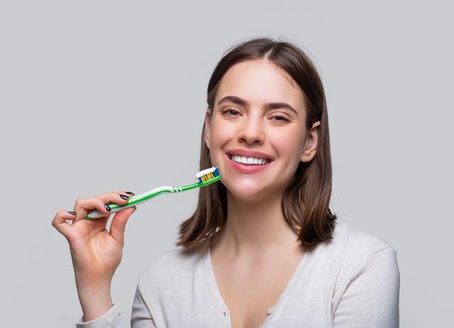 a woman is brushing her teeth with a green toothbrush .
