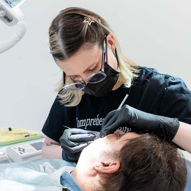 a woman wearing glasses and a mask is working on a man 's eyebrows .