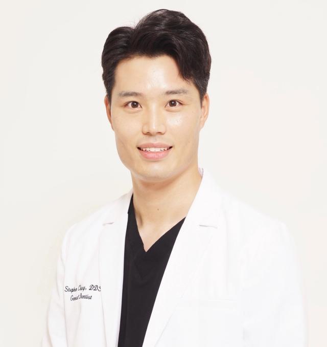a man in a white lab coat and black scrubs is smiling for the camera .