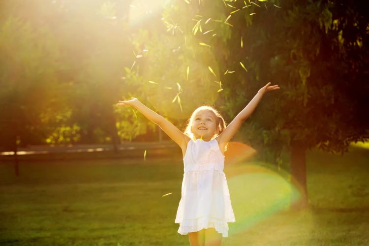 a little girl in a white dress is throwing leaves in the air in a park .