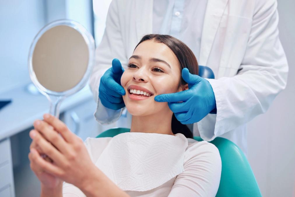a woman is sitting in a dental chair looking at her teeth in a mirror .