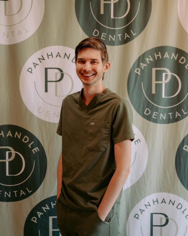 Smiling young man in green scrubs against a Panhandle Dental logo backdrop.