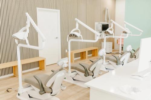 Three modern dental chairs with lights and equipment in a bright office with wood-paneled walls and benches.