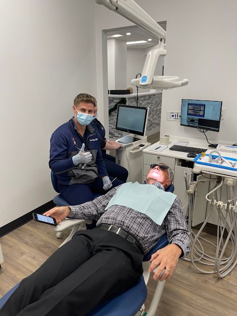 a man is laying in a dental chair while a dentist looks on .