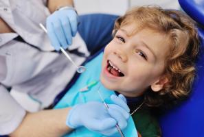 Smiling young boy in a dental chair with a dentist examining his teeth.