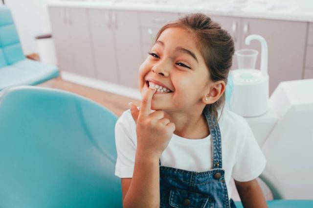 A happy child pointing to her teeth in a dental chair.